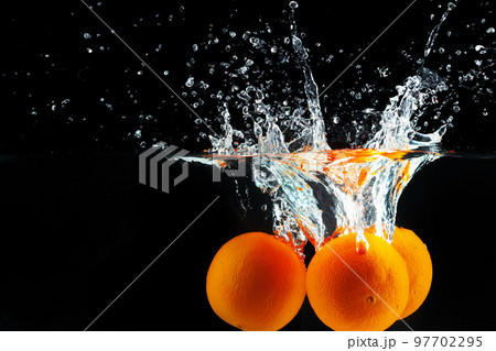 Oranges falling into water against black background, studio shot 97702295