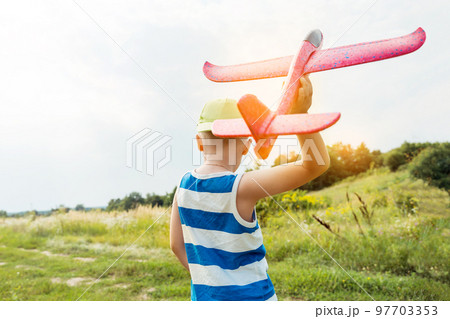 Boy holding toy airplane and preparing to launch it into the sky outdoors. Happy childhood, dreaming concept. Boy holding toy airplane and preparing to launch it into the sky outdoors. Happy childhood, dreaming concept. 97703353