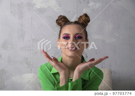 Portrait of young woman with bright makeup and bun hairstyle in green shirt. Gray background. Portrait of young woman with bright makeup and bun hairstyle in green shirt. Gray background. 97703774
