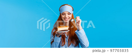 Waist-up portrait cheerful and delighted young caucasian redhead woman in pyjama and sleep mask, holding slice cake and spoon smiling delighted, looking at tasty dessert, wear nightwear Waist-up portrait cheerful and delighted young caucasian redhead woman in pyjama and sleep mask, holding slice cake and spoon smiling delighted, looking at tasty dessert, wear nightwear 97703835