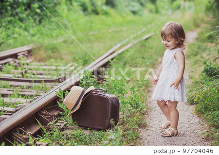 Charming baby with a suitcase walks along the railroad 97704046
