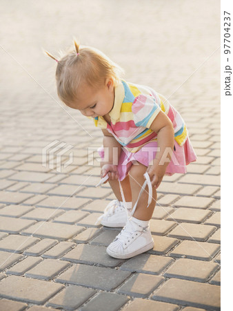 fair-haired baby in tennis clothes ties shoelaces at sunset 97704237