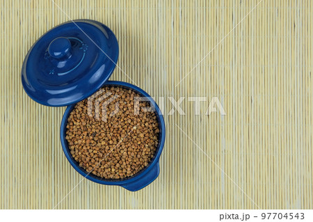 Buckwheat in in blue bowl on a straw background. Vegetarian organic product. Vintage view. Top view. Copy space. 97704543