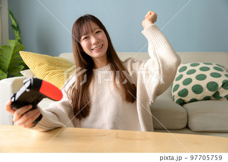 リビングでゲームする女性　ゲーム女子　ゲームコントローラー　休日ライフスタイル　ガッツポーズ　自然光 97705759