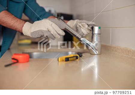 Close up of male plumber repair sink faucet at kitchen. Good quality plumbing company service Close up of male plumber repair sink faucet at kitchen. Good quality plumbing company service 97709251