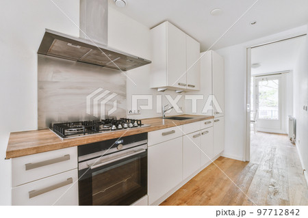 Fragment of interior of light narrow home kitchen with minimalist style white furniture with sink and stove Fragment of interior of light narrow home kitchen with minimalist style white furniture with sink and stove 97712842