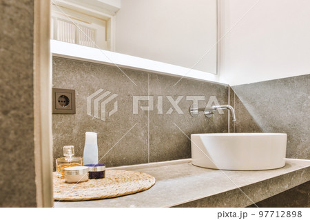 Sink with tap and liquid soap hanging on tiled wall under mirror in contemporary restroom at home Sink with tap and liquid soap hanging on tiled wall under mirror in contemporary restroom at home 97712898