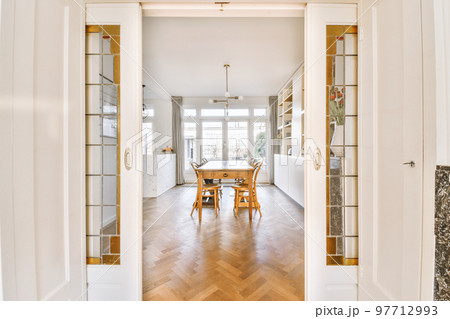 Interior of spacious light dining room with elegant chandelier located near kitchen with comfortable furniture and appliances 97712993