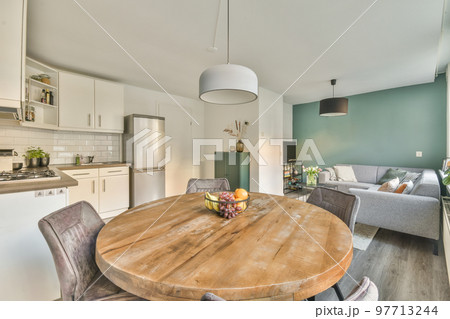 Table with chairs and flowers located near lounge area and kitchen in spacious room of contemporary apartment 97713244