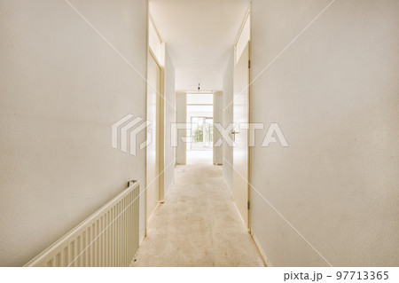 Light narrow hallway with many doors in white walls and glowing lamp over lumber floor 97713365