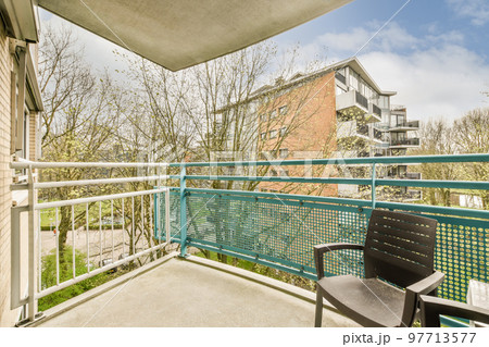 Narrow brick balcony with metal railings, wooden chair and door with glass leads to the kitchen 97713577