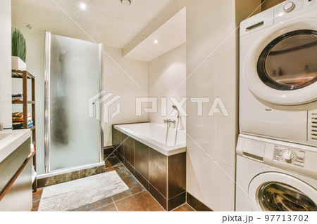 Sinks with mirrors and clean bathtub located near shower box with glass door in modern bathroom with white tiled walls 97713702