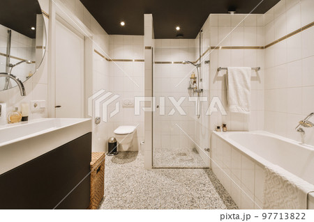 Sinks with mirrors and clean bathtub located near shower box with glass door in modern bathroom with white tiled walls Sinks with mirrors and clean bathtub located near shower box with glass door in modern bathroom with white tiled walls 97713822