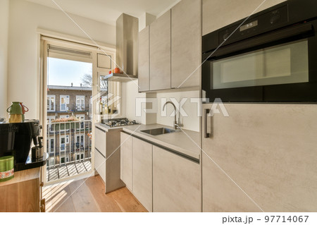 Light small home kitchen with wide window furnished with cupboards and shelves with appliances in modern urban apartment Light small home kitchen with wide window furnished with cupboards and shelves with appliances in modern urban apartment 97714067