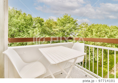 Narrow brick balcony with metal railings, wooden chair and door 97714101