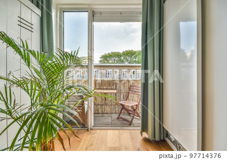 Narrow brick balcony with metal railings, wooden chair and door 97714376