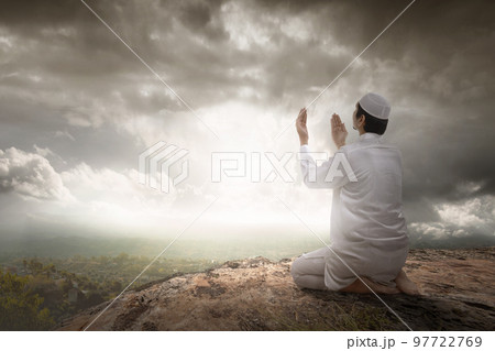 Rear view of a Muslim man sitting while raised hands and praying Rear view of a Muslim man sitting while raised hands and praying 97722769