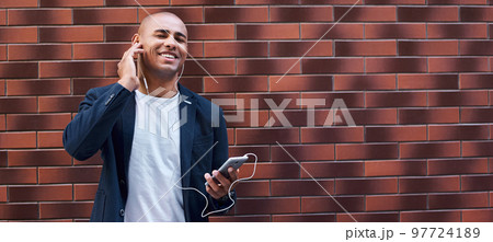 Music lover. Young guy wearing earphones standing on wall listening to music on smartphone closed eyes smiling cheerful Music lover. Young guy wearing earphones standing on wall listening to music on smartphone closed eyes smiling cheerful 97724189