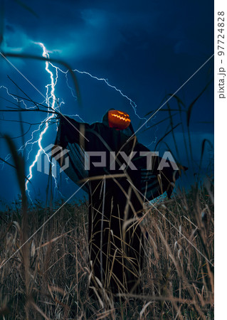 A scary scarecrow with a pumpkin head in a night corn field during a thunderstorm. 97724828