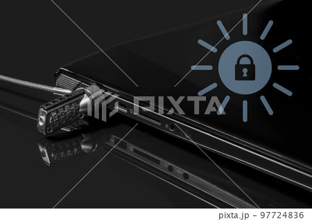 The laptop is locked with a cable lock on surface of dark mirror. Safety concept. Kensington Security Slot The laptop is locked with a cable lock on surface of dark mirror. Safety concept. Kensington Security Slot 97724836