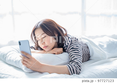 ベッドでスマホの画面を見つめ寝落ちする女性 97727123