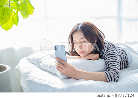 ベッドでスマホの画面を見つめ寝落ちする女性 97727124
