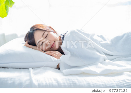 明るいシンプルな部屋のベッドで眠る女性 97727125