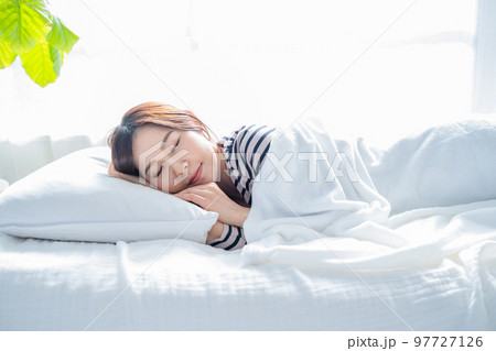 明るいシンプルな部屋のベッドで眠る女性 97727126