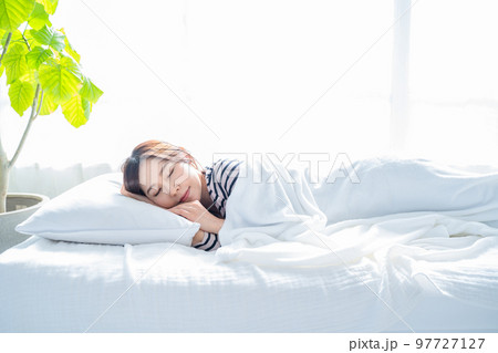 明るいシンプルな部屋のベッドで眠る女性 97727127