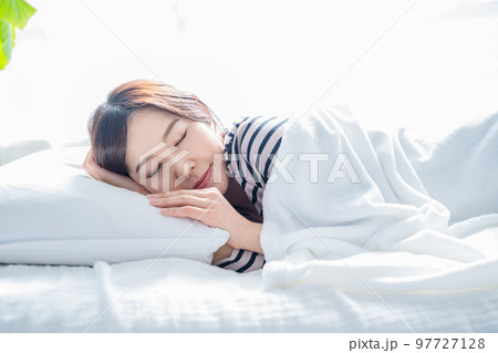 明るいシンプルな部屋のベッドで眠る女性 97727128