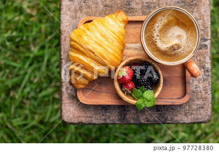 Coffee cup and croissant on outside garden table Coffee cup and croissant on outside garden table 97728380
