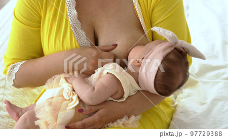 Young woman breastfeeding her baby while sitting on bed Young woman breastfeeding her baby while sitting on bed 97729388