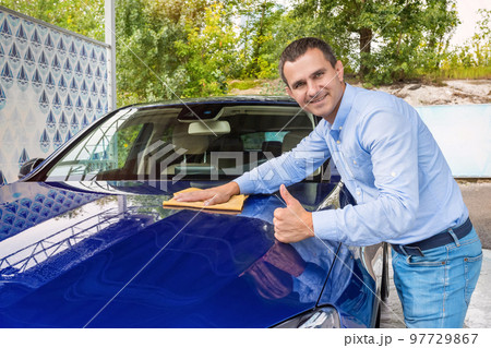 Man polishing car on a car wash. The man holds the microfiber in hand and polishes the car 97729867