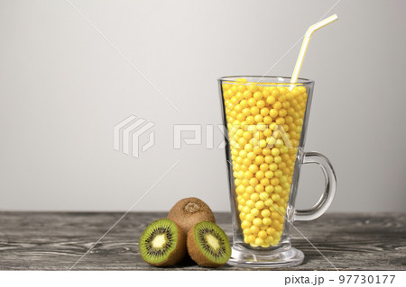The glass goblet is filled with vitamins in the form of dragees. Kiwi halves nearby. On black pine boards. On a white background. 97730177