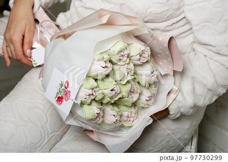 Marshmallow bouquet. Zephyr tulips. Natural homemade marshmallow. Packed in paper in the form of a bouquet. In the hands of a woman. Close-up. Marshmallow bouquet. Zephyr tulips. Natural homemade marshmallow. Packed in paper in the form of a bouquet. In the hands of a woman. Close-up. 97730299