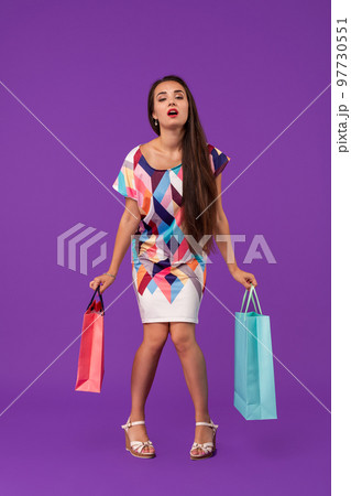 Lady with tired face. Girl stands on purple background holding shopping bags. Woman wears fashionable dress. 97730551