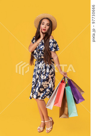 Fashion portrait young woman wearing a shopping bags, straw hat, dress posing over colorful yellow background 97730666