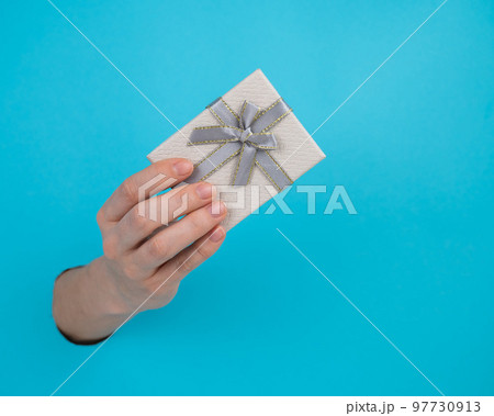 A woman's hand sticks out of a blue paper background and a gift box. A woman's hand sticks out of a blue paper background and a gift box. 97730913