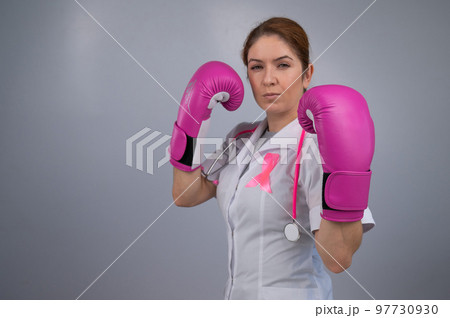 Serious female doctor in pink boxing gloves with a pink ribbon on a gray background. Fight against breast cancer.  97730930