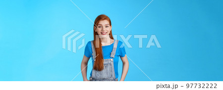Cheerful glad redhead woman standing joyful relaxed pose, wear denim dungaress over t-shirt summer outfit, smiling pleased, carefree friendly conversation, pose blue background 97732222