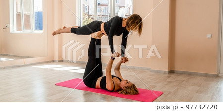 Steam yoga of two women doing yoga indoors. One woman holding the other with her arms and legs 97732720