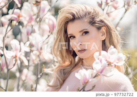 Portrait of a beautiful happy middle aged woman enjoying the smell in a blooming spring garden. Beautiful magnolia bushes, large flowers. 97732722