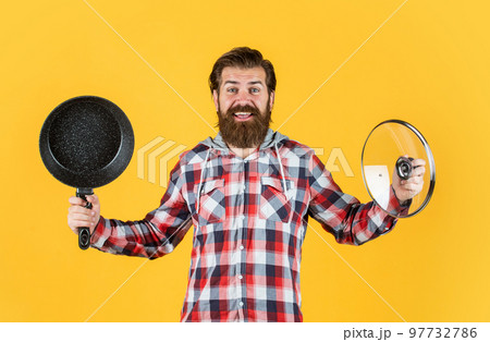 male hipster with fashionable groomed hair and beard cooking with pan, kitchen male hipster with fashionable groomed hair and beard cooking with pan, kitchen 97732786