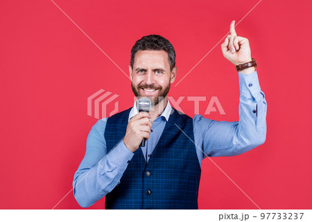 Happy man with unshaven facial hair speak into microphone keeping index finger raised, idea Happy man with unshaven facial hair speak into microphone keeping index finger raised, idea 97733237