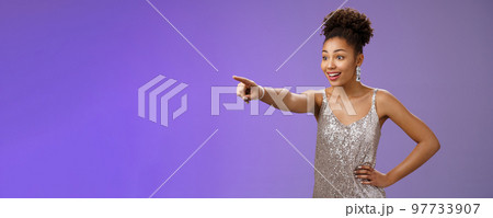 Impressed fascinated cute african-american woman excited pointing index finger sideways thrilled enjoying incredible exhibition standing excited blue background, glancing amused Impressed fascinated cute african-american woman excited pointing index finger sideways thrilled enjoying incredible exhibition standing excited blue background, glancing amused 97733907