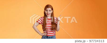 Lively friendly redhead woman discuss new trend pointing upper left corner, smiling, talking joyfully, hold hand chest relaxed casual pose, stand orange background cheerful show advertisement Lively friendly redhead woman discuss new trend pointing upper left corner, smiling, talking joyfully, hold hand chest relaxed casual pose, stand orange background cheerful show advertisement 97734313
