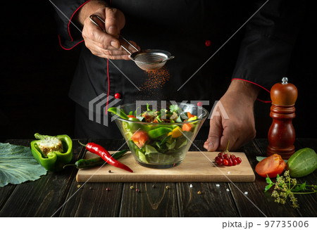 The chef adds flavoring to the vegetable salad. Vegetarian food by hands of the cook in the kitchen. Menu idea for a hotel or restaurant The chef adds flavoring to the vegetable salad. Vegetarian food by hands of the cook in the kitchen. Menu idea for a hotel or restaurant 97735006