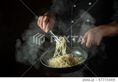 The chef cooks spaghetti in a hot pan. Space for advertising on a black background. Italian national cuisine The chef cooks spaghetti in a hot pan. Space for advertising on a black background. Italian national cuisine 97735009