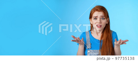 Puzzled confused redhead cute woman look ambushed, raise hands shrugging uncertain, frowning perplexed, cannot understand what happened, stand frustrated upset blue background 97735138