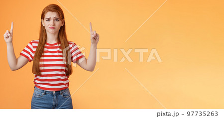 Disappointed upset cute whining timid redhead girl, gloomy face, pulling sad expression, complain, crying feeling regret loss, losing lottery, pointing up displeased, show despair and sorrow emotion 97735263